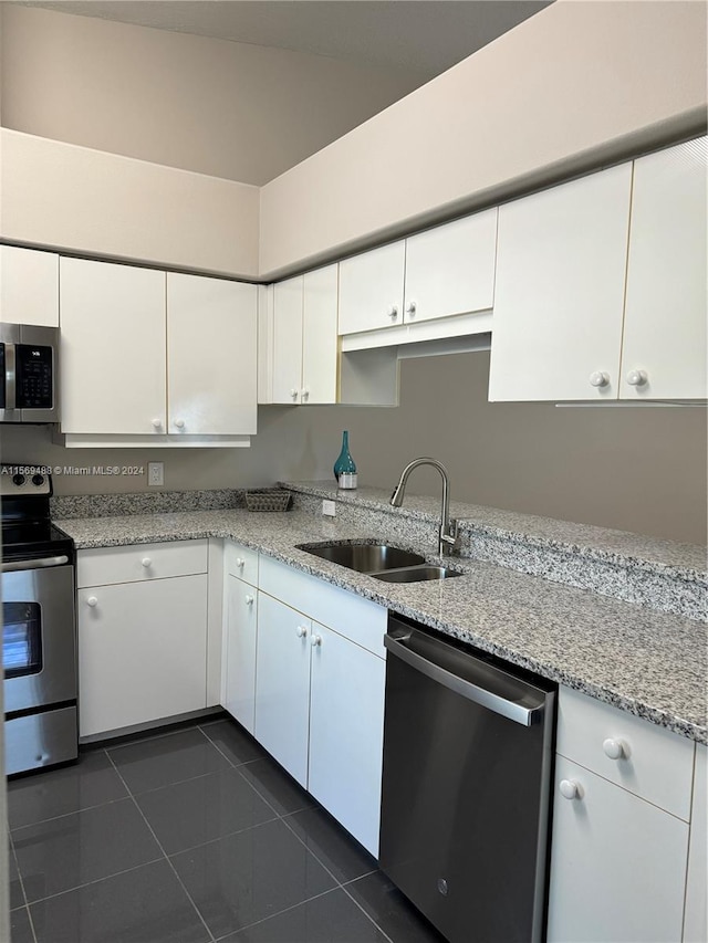 kitchen featuring light stone countertops, stainless steel appliances, dark tile flooring, white cabinets, and sink