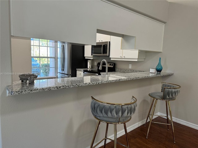 kitchen with light stone counters, appliances with stainless steel finishes, kitchen peninsula, and dark hardwood / wood-style floors