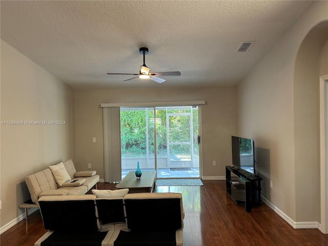 living room with dark wood-type flooring, ceiling fan, and a textured ceiling