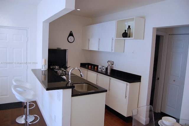 kitchen with sink, white cabinetry, dark hardwood / wood-style floors, kitchen peninsula, and a kitchen breakfast bar