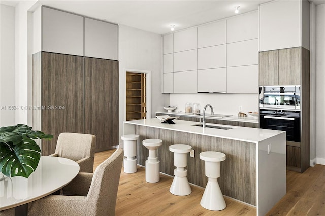 kitchen with a center island with sink, light hardwood / wood-style flooring, a breakfast bar, and sink