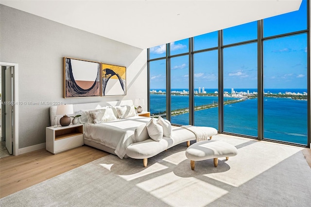 bedroom featuring light hardwood / wood-style flooring, access to exterior, a wall of windows, and a water view