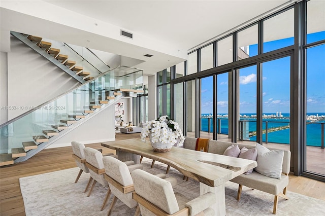 dining space with a water view, light hardwood / wood-style flooring, and a wall of windows