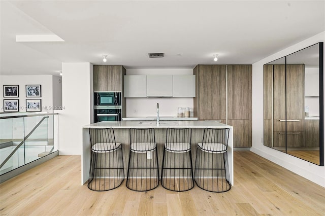 kitchen featuring built in microwave, a center island with sink, light hardwood / wood-style floors, and stainless steel oven