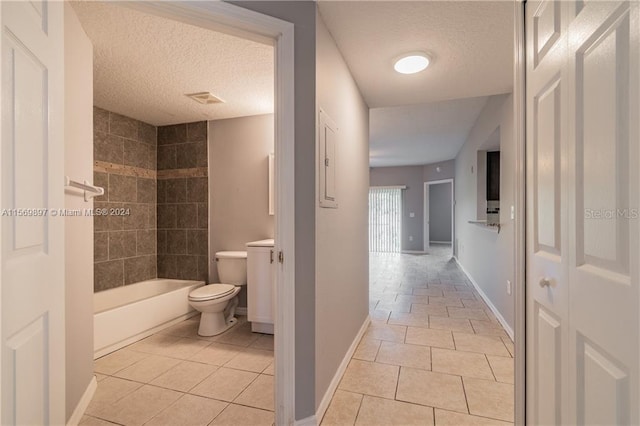 bathroom featuring toilet, tile flooring, tiled shower / bath combo, and a textured ceiling