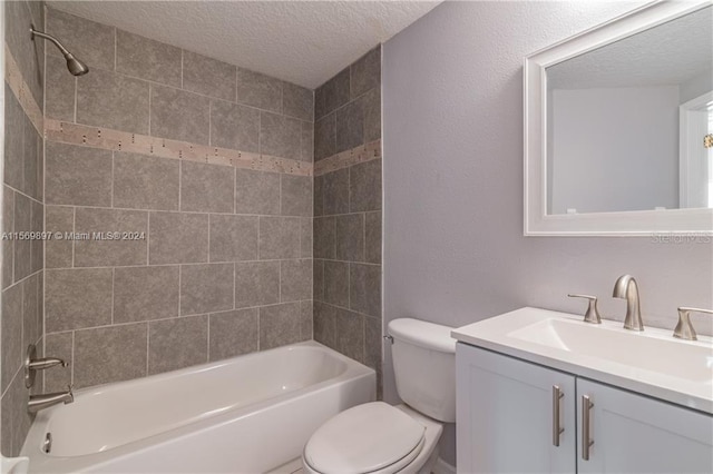 full bathroom with tiled shower / bath, vanity, toilet, and a textured ceiling