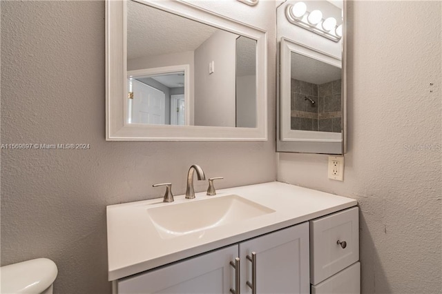 bathroom with a textured ceiling, vanity, and toilet