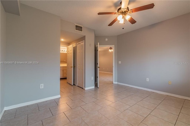 unfurnished bedroom with ensuite bathroom, ceiling fan, a closet, and light tile flooring