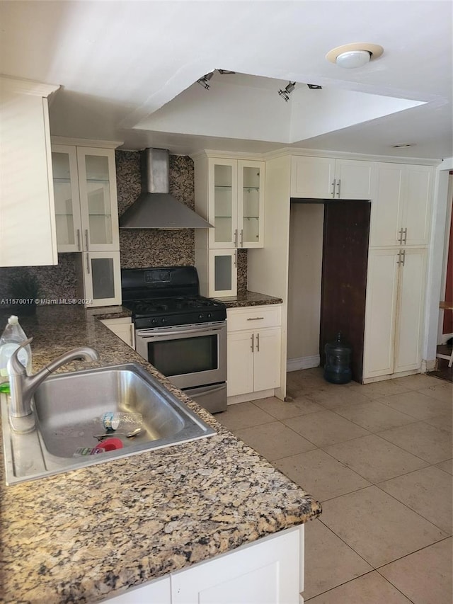 kitchen featuring stainless steel gas range oven, backsplash, wall chimney range hood, sink, and light tile floors