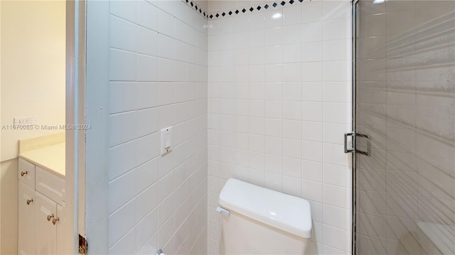 bathroom with tiled shower, vanity, toilet, and tile walls