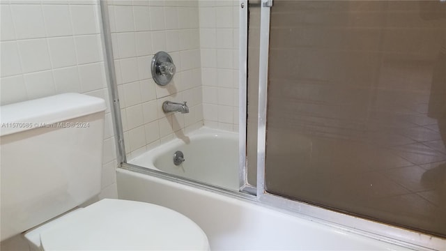 bathroom with tile walls, toilet, and enclosed tub / shower combo