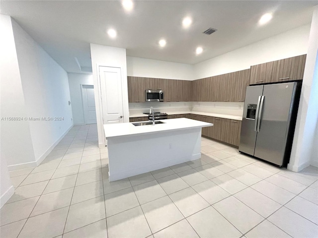 kitchen featuring appliances with stainless steel finishes, light tile floors, sink, and an island with sink