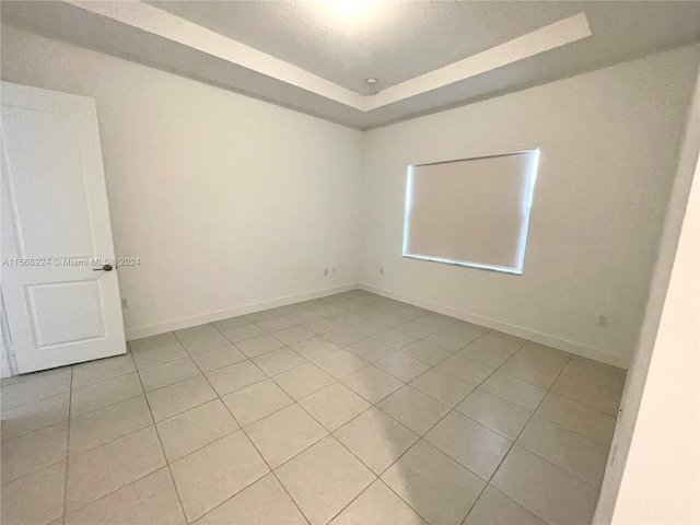 spare room with a raised ceiling and light tile floors