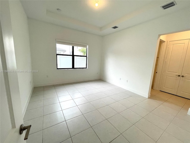 tiled empty room featuring a raised ceiling