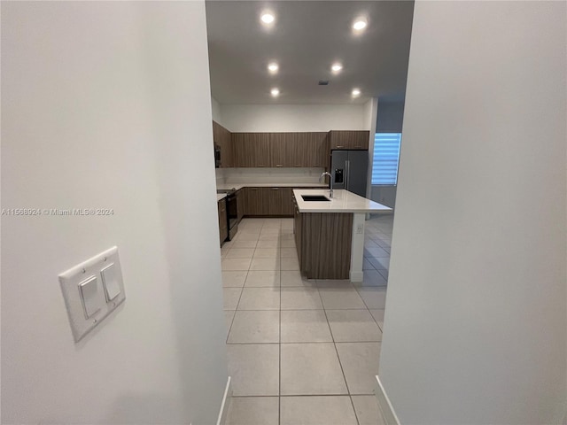 kitchen featuring stainless steel fridge with ice dispenser, light tile floors, sink, and an island with sink