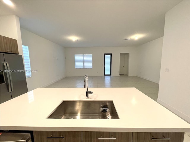 kitchen featuring light tile floors, stainless steel refrigerator with ice dispenser, sink, and an island with sink