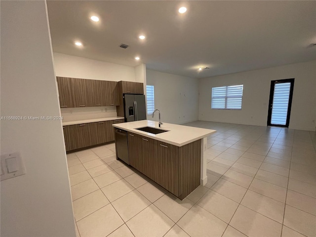 kitchen with sink, dishwasher, light tile flooring, stainless steel fridge with ice dispenser, and an island with sink