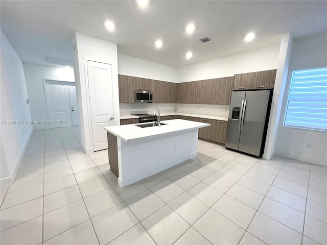 kitchen with sink, stainless steel appliances, light tile floors, and a kitchen island with sink