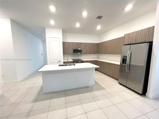 kitchen with sink, stainless steel appliances, light tile flooring, and an island with sink