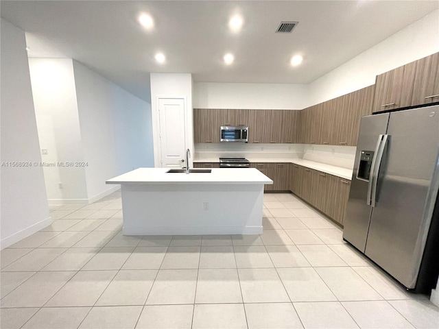 kitchen featuring stainless steel appliances, light tile floors, sink, and an island with sink