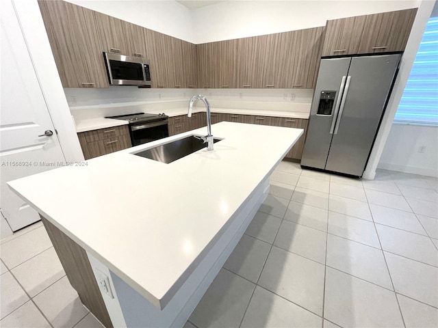 kitchen featuring sink, stainless steel appliances, light tile floors, and an island with sink