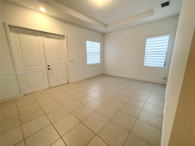 unfurnished bedroom with light tile flooring, a tray ceiling, a closet, and multiple windows