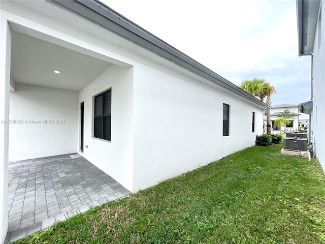 view of side of home with a patio area, a yard, and central AC