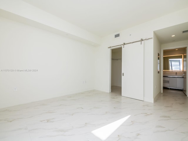 unfurnished bedroom featuring ensuite bath, a walk in closet, light tile floors, and a barn door