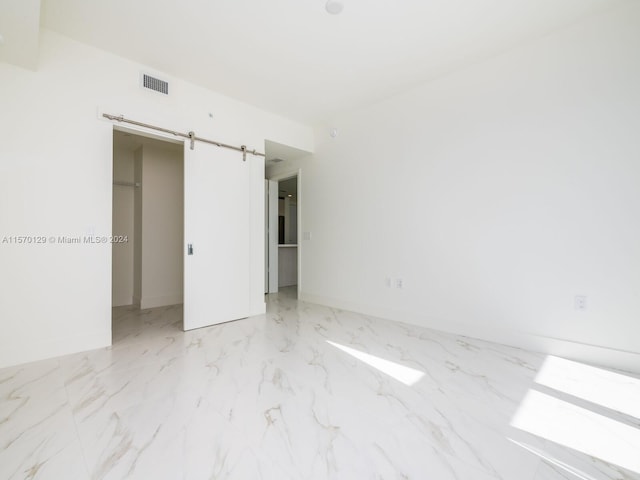 unfurnished bedroom featuring a closet, light tile floors, and a barn door