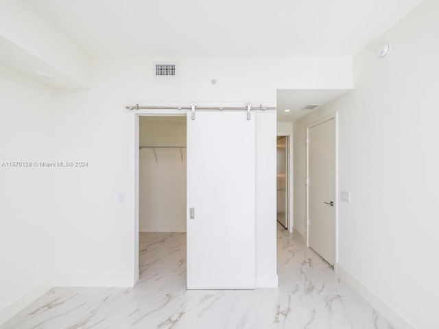 interior space with a barn door, a closet, a walk in closet, and light tile flooring