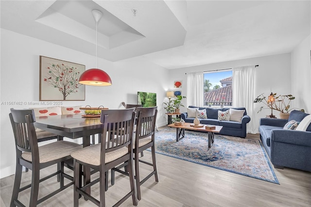 dining space with a tray ceiling and light wood-type flooring