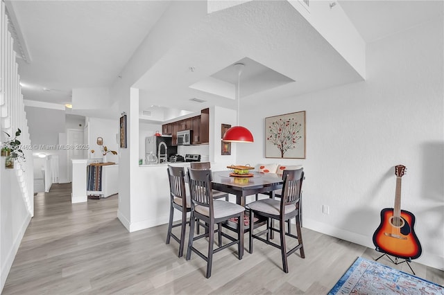 dining space with a raised ceiling and light wood-type flooring