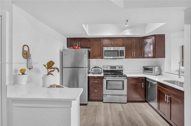 kitchen with appliances with stainless steel finishes, dark brown cabinetry, a tray ceiling, sink, and light hardwood / wood-style flooring