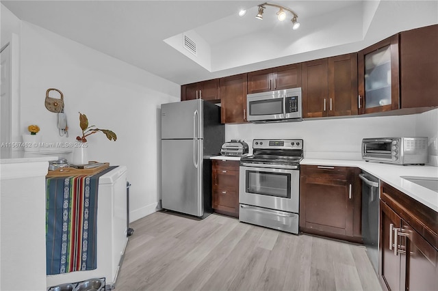 kitchen with dark brown cabinets, appliances with stainless steel finishes, and light hardwood / wood-style flooring