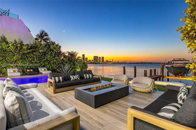 deck at dusk with an outdoor living space with a fire pit and a water view