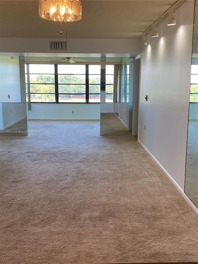 unfurnished room with a textured ceiling, baseboards, visible vents, carpet, and track lighting