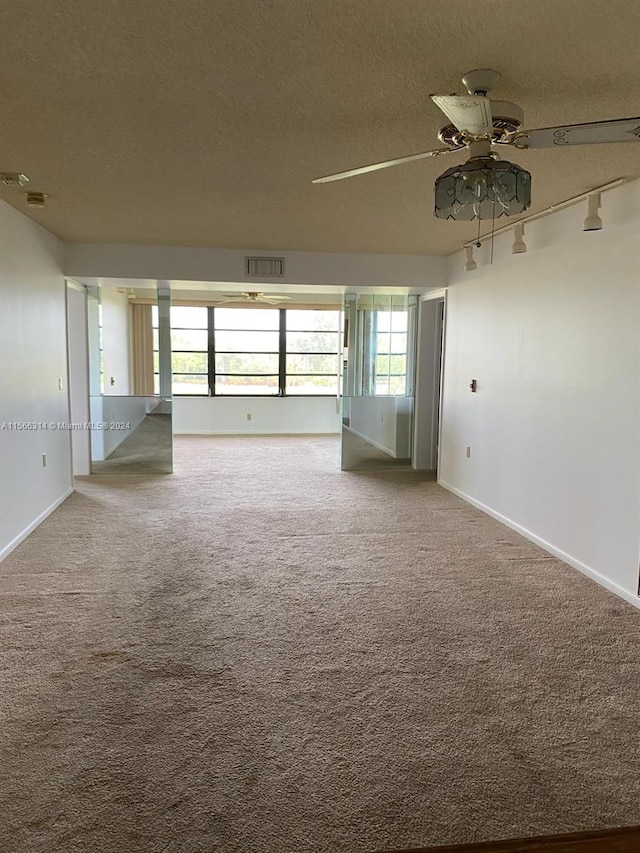 empty room featuring ceiling fan, carpet floors, track lighting, and a textured ceiling