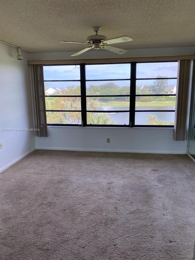 carpeted empty room featuring ceiling fan, a textured ceiling, a healthy amount of sunlight, and a water view