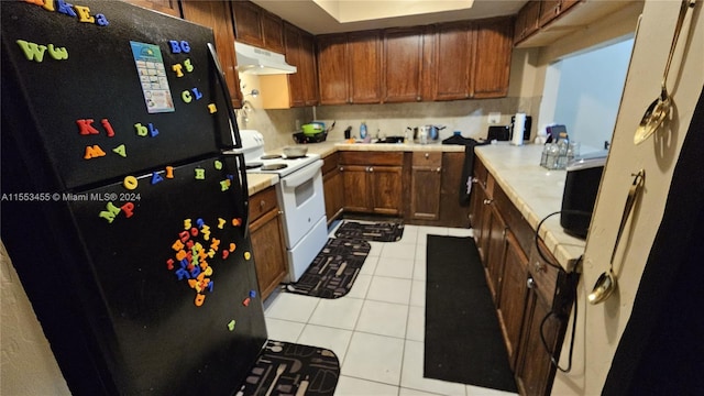 kitchen with black refrigerator, white range with electric stovetop, light tile floors, and tasteful backsplash