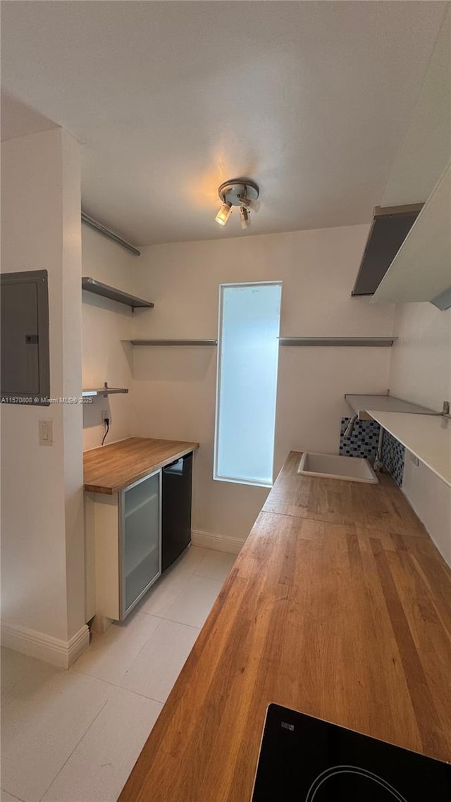 interior space with electric panel, sink, butcher block counters, light tile patterned floors, and dishwasher