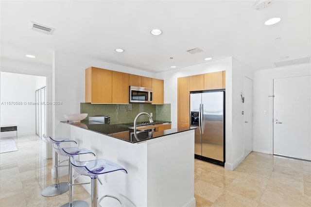 kitchen featuring appliances with stainless steel finishes, light tile floors, a kitchen bar, backsplash, and kitchen peninsula