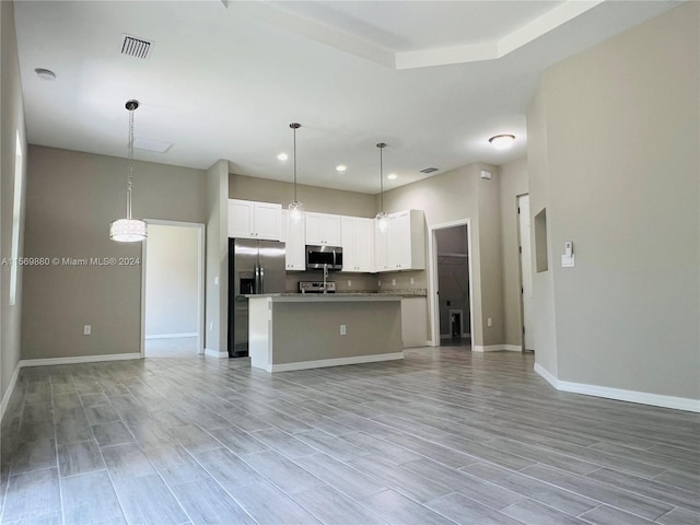 kitchen with light wood-type flooring, stainless steel appliances, white cabinets, hanging light fixtures, and an island with sink