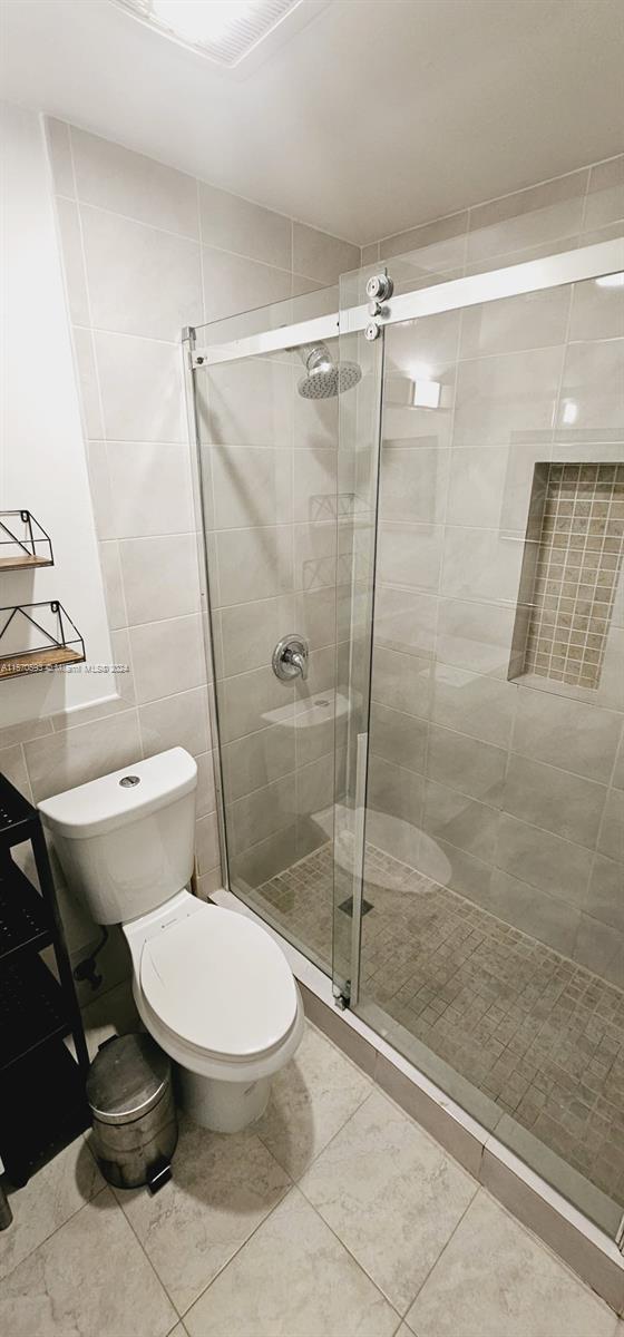 bathroom featuring a shower with door, tile floors, tile walls, and toilet