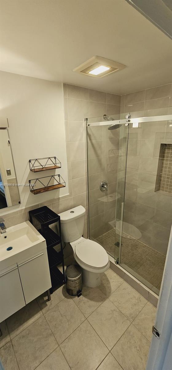 bathroom featuring a shower with door, vanity, toilet, and tile flooring