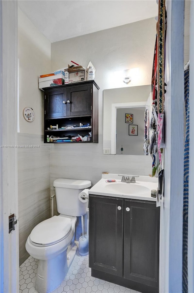 bathroom with toilet, tile flooring, tile walls, and large vanity