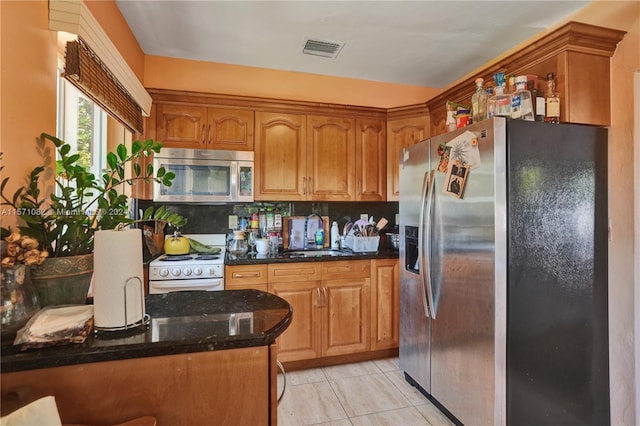 kitchen featuring appliances with stainless steel finishes, sink, backsplash, light tile flooring, and dark stone countertops