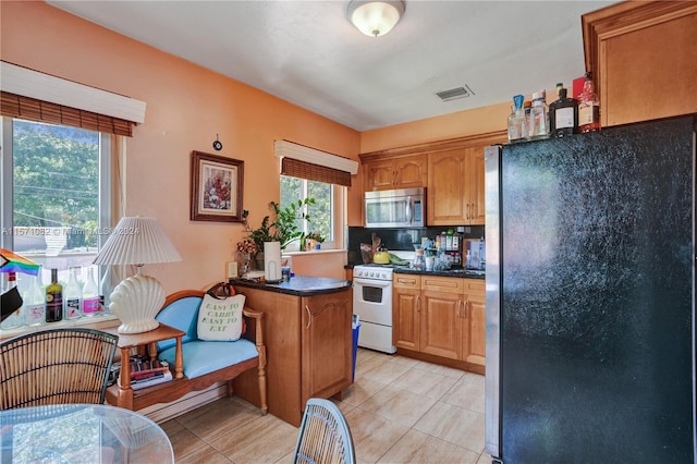 kitchen with black refrigerator, tasteful backsplash, white range with gas cooktop, and light tile floors