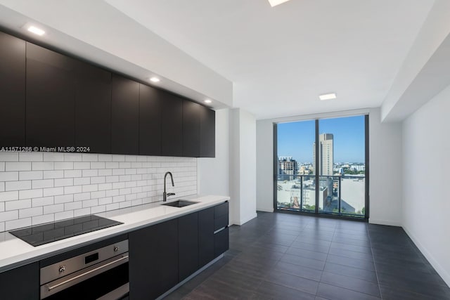 kitchen featuring sink, tasteful backsplash, black electric cooktop, stainless steel oven, and a wall of windows