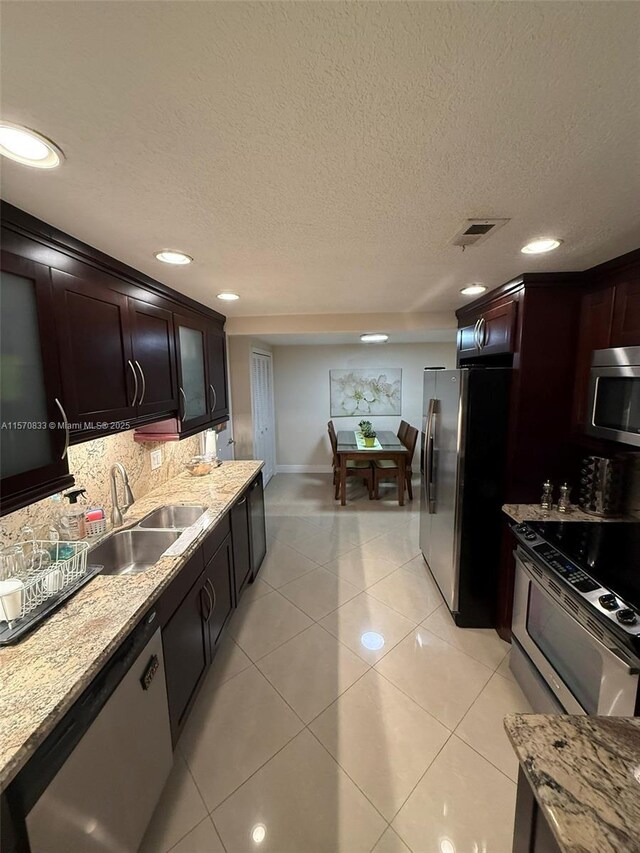 kitchen featuring stainless steel appliances, light stone countertops, light tile patterned floors, and sink