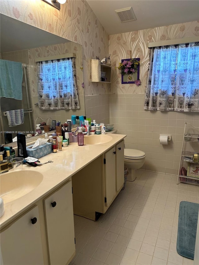 bathroom featuring double vanity, toilet, tile flooring, and tile walls